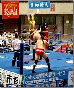 リング上で2人の選手が戦っており、うち1人の選手が相手選手をさかさまに持ち上げ落そうとしている試合中の写真